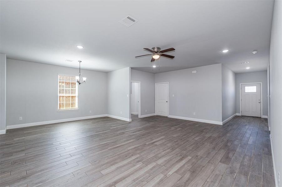 Spare room with ceiling fan with notable chandelier, wood finished floors, visible vents, and baseboards