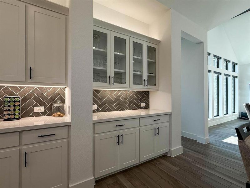 Butler's Pantry area featuring backsplash, light stone counters, glass insert cabinets, dark wood-type flooring, and vaulted ceiling Butler's Pantry area featuring backsplash, light stone counters, glass insert cabinets, dark wood-type flooring, and vaulted ceiling