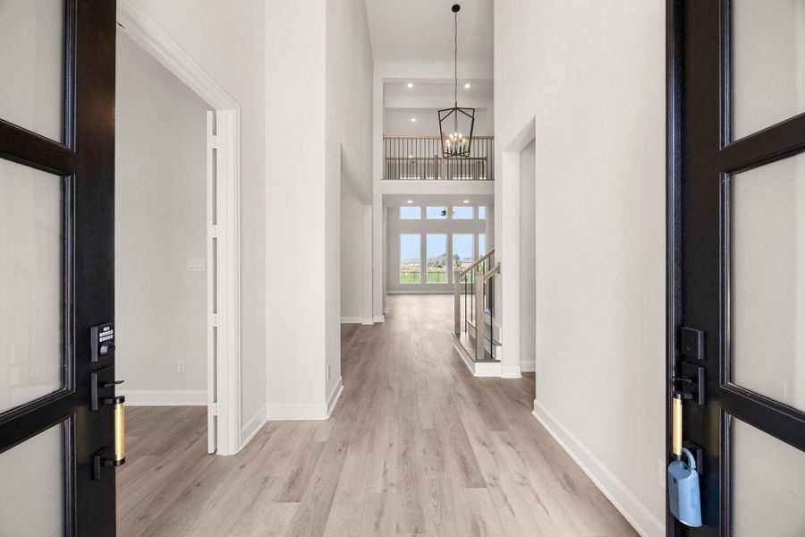 Spectacular grand foyer offering an immediate view of the home's open-concept luxury. Stepping through the dramatic double front doors, guests are greeted by soaring two-story ceilings, a large designer lantern chandelier, and premium wide-plank wood-look flooring. The expansive entry provides a direct sightline past the modern split-staircase and upper catwalk straight through to the massive wall of windows in the main family room. Spectacular grand foyer offering an immediate view of the home's open-concept luxury. Stepping through the dramatic double front doors, guests are greeted by soaring two-story ceilings, a large designer lantern chandelier, and premium wide-plank wood-look flooring. The expansive entry provides a direct sightline past the modern split-staircase and upper catwalk straight through to the massive wall of windows in the main family room.