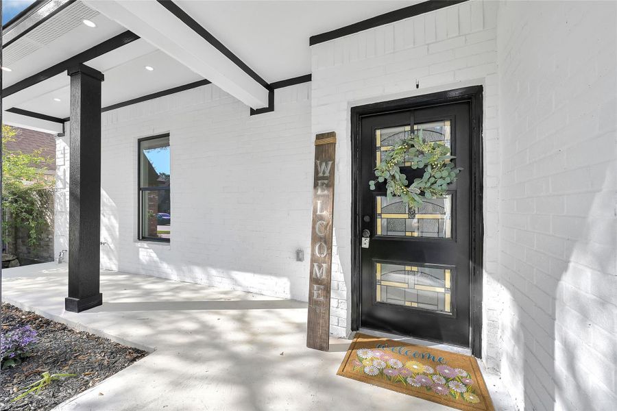 This welcoming front porch features a stylish black door with decorative glass panels. The white brick exterior and contrasting black beams create a modern and inviting entrance.
