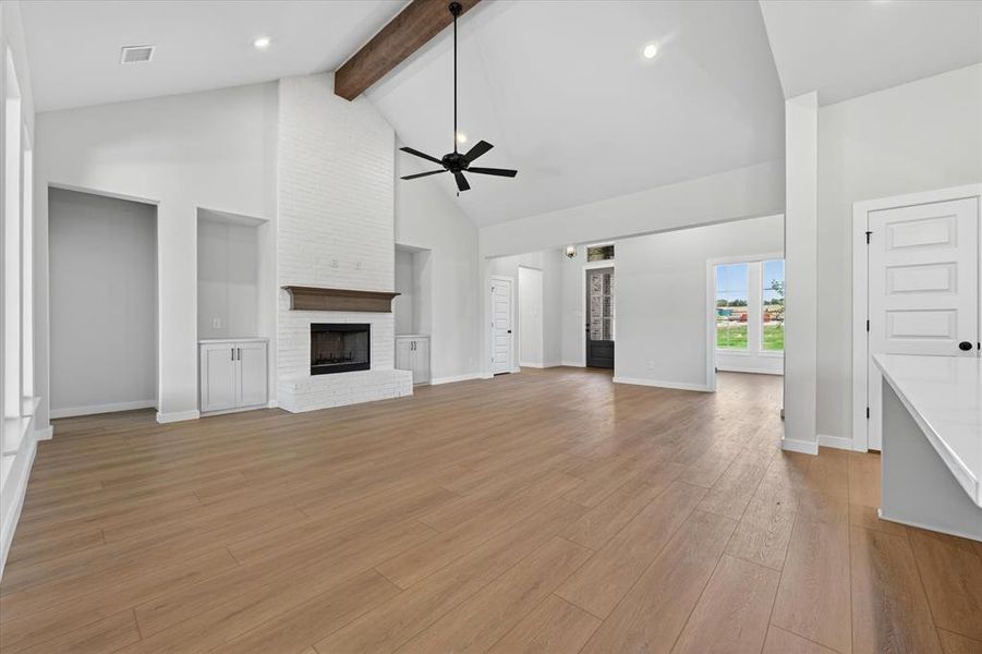 Vaulted ceiling with exposed wood beam, white brick fireplace with wood mantel, built-in cabinetry, wood-finish flooring, and recessed lighting