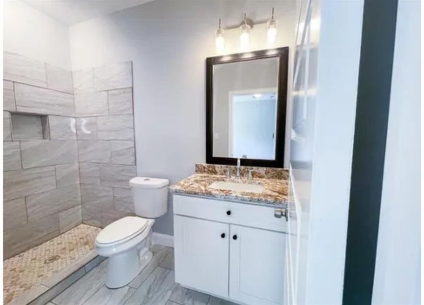 Bathroom with vanity, tile flooring, toilet, and tiled shower Bathroom with vanity, tile flooring, toilet, and tiled shower