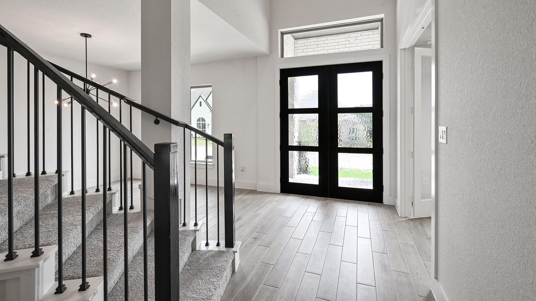 Entryway featuring a textured wall, french doors, stairs, wood finished floors, and a towering ceiling