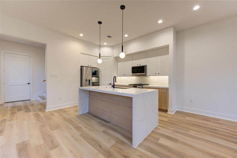 This stunning kitchen features upgraded quartz countertops (2" thick laminated edges), large pantry, waterfall island, sleek modern cabinetry, and stainless steel smart appliances, including the craft ice refrigerator!