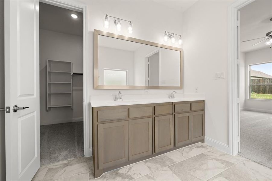 Full bath with marble look tiles, ceiling fan, and double vanity