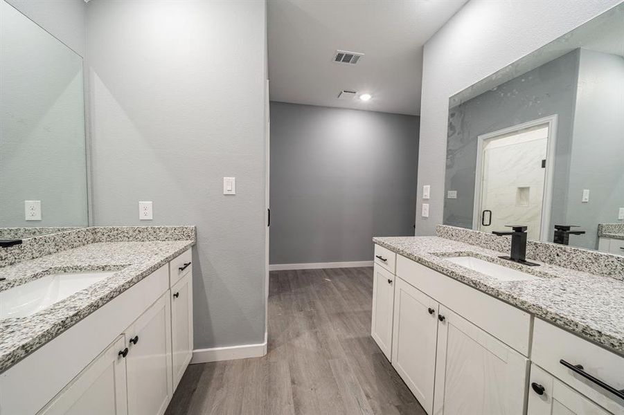Full bathroom with two vanities, dark wood-style flooring, a shower stall, and a textured wall Full bathroom with two vanities, dark wood-style flooring, a shower stall, and a textured wall