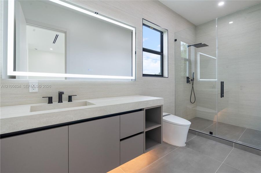Floating vanity with integrated sink, stone-finish countertop, under-cabinet lighting, LED-backlit mirror, and glass-enclosed walk-in shower with matte black rainfall fixture