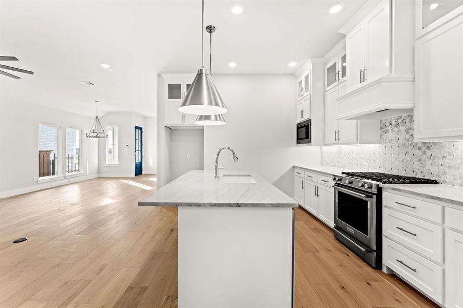 Kitchen featuring stainless steel range, sink, white cabinets, and pendant lighting