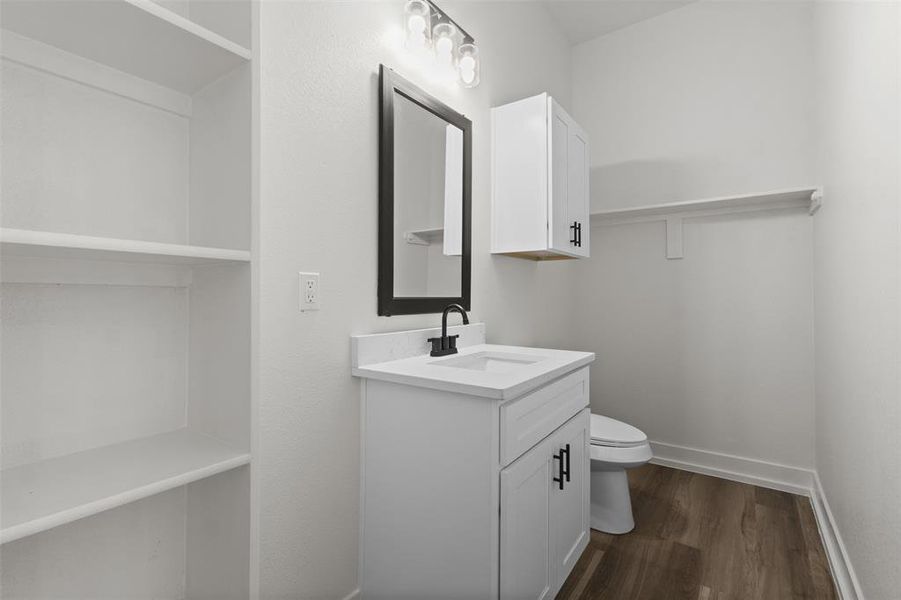 The bathroom features a vanity with a white countertop and a rectangular sink, complemented by a black-framed mirror and modern lighting