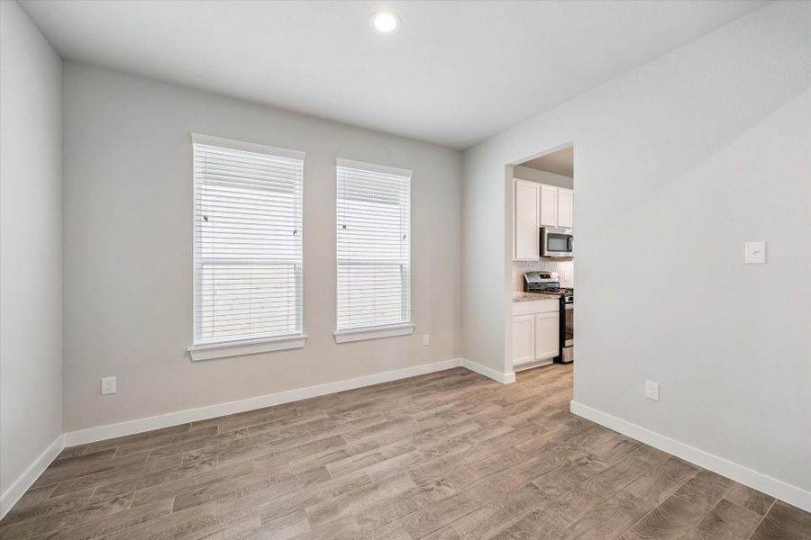 This room features light wood flooring, neutral walls, and two large windows providing natural light. It opens into a kitchen with modern appliances and white cabinetry. Ideal for a dining space. This room features light wood flooring, neutral walls, and two large windows providing natural light. It opens into a kitchen with modern appliances and white cabinetry. Ideal for a dining space.
