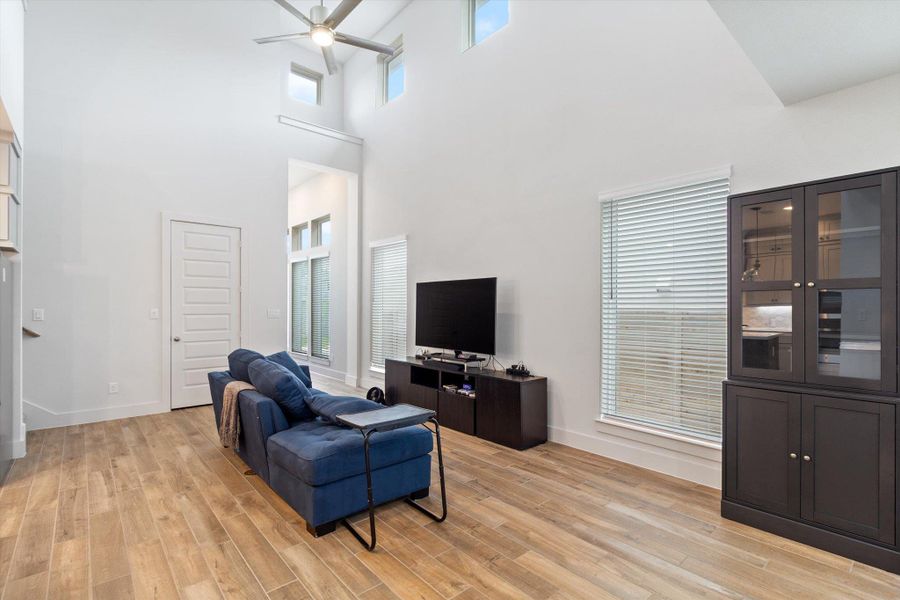 Living room featuring a ceiling fan, light wood-style floors, and a towering ceiling