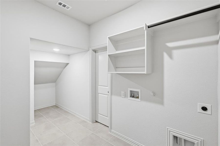 Laundry area with hookup for a gas dryer, hookup for a washing machine, electric dryer hookup, light tile patterned flooring, and lofted ceiling