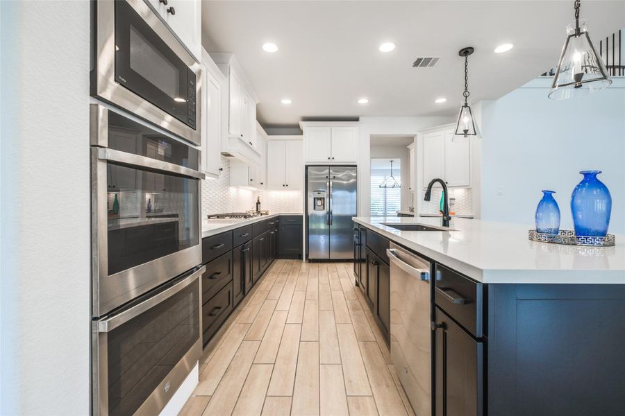 A true dream kitchen! Gleaming quartz , high-end stainless steel appliances, stylish modern lighting, an island with storage, spacious walk-in pantry beautiful countertops & backsplash, paired with chic dark cabinets