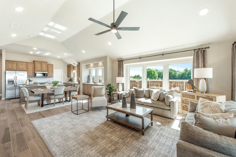 Open-concept living room with vaulted ceiling, ceiling fan, and views into dining area and kitchen