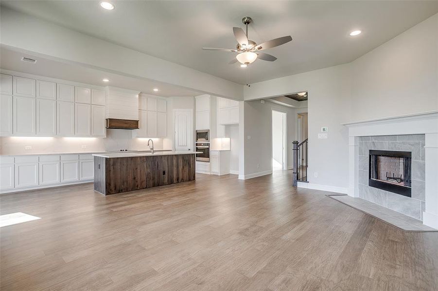 Kitchen with oven, light hardwood / wood-style flooring, white cabinetry, and an island with sink