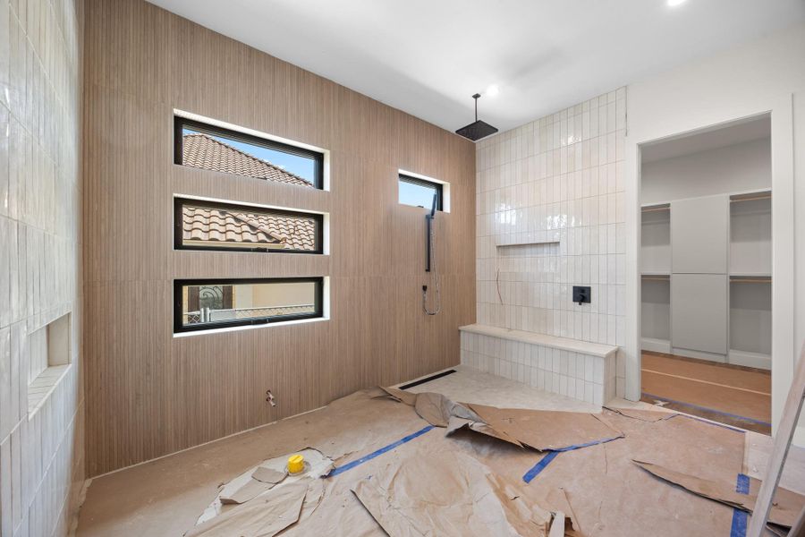 Spacious shower area featuring light wood-finish wall paneling, three horizontal windows with black framing, and a tiled shower wall with a built-in bench and recessed niche