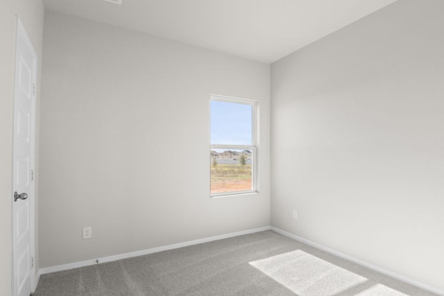 Image of a bedroom with tan carpeting and light grey walls with a window