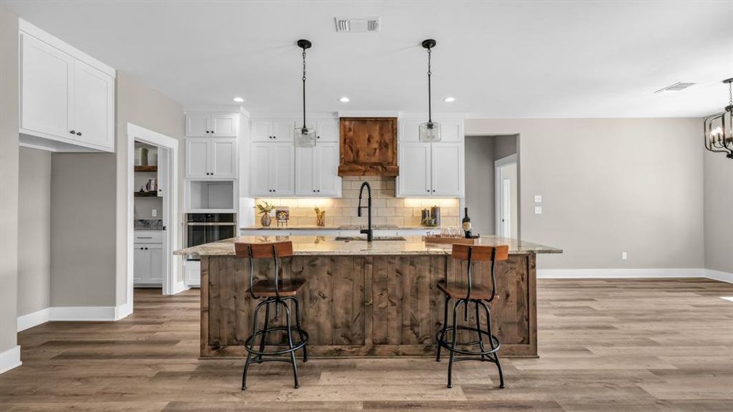 Kitchen featuring decorative light fixtures, a large island with seating, white cabinets, and granite countertops