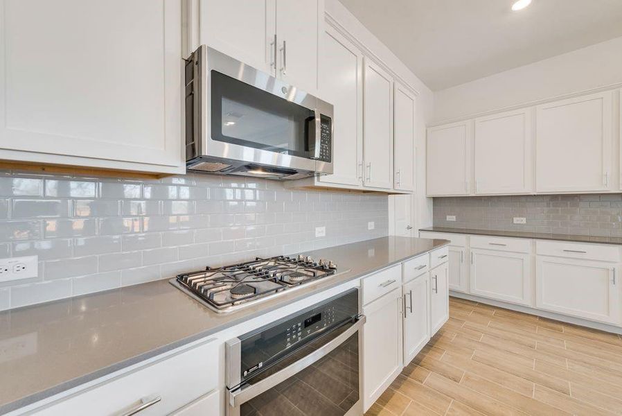 Kitchen featuring appliances with stainless steel finishes, white cabinetry, tasteful backsplash, light wood-style flooring, and recessed lighting