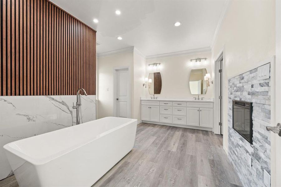 Full bathroom featuring double vanity, a freestanding tub, ornamental molding, a stone fireplace, and recessed lighting Full bathroom featuring double vanity, a freestanding tub, ornamental molding, a stone fireplace, and recessed lighting