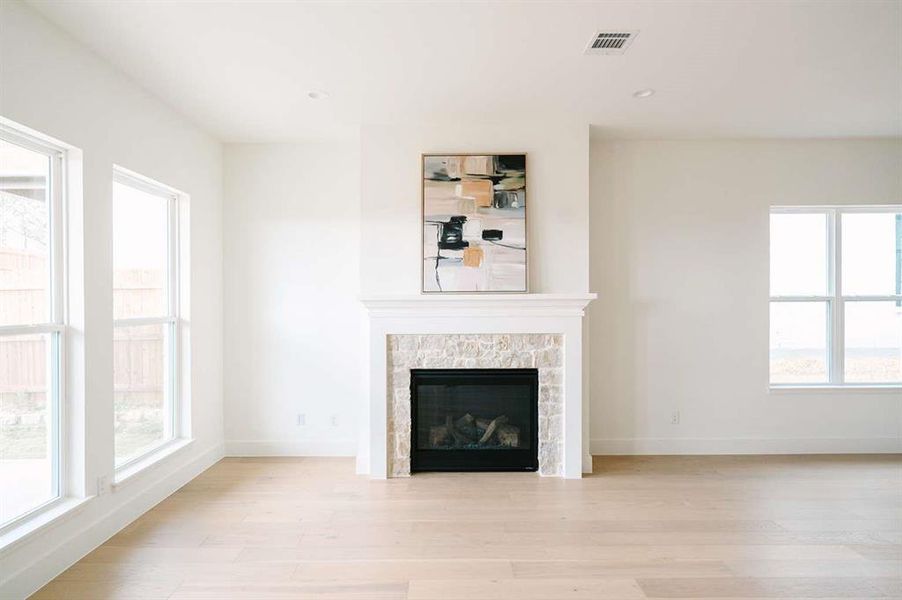 Unfurnished living room with light wood-type flooring, a stone fireplace, and plenty of natural light