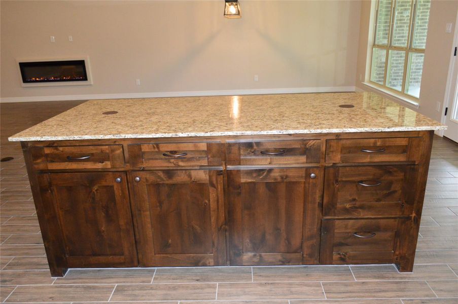 Kitchen with wood finish floors, light stone counters, and a warm lit fireplace