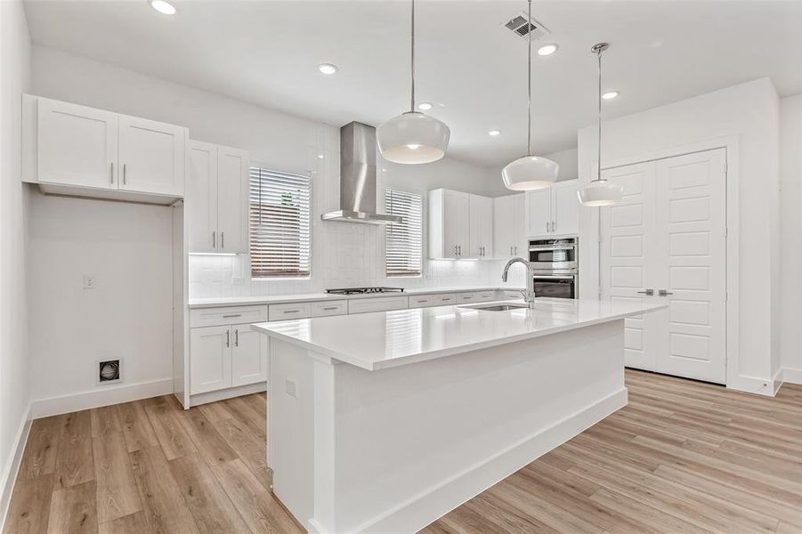 Kitchen featuring an island with sink, white cabinetry, backsplash, hanging light fixtures, and recessed lighting