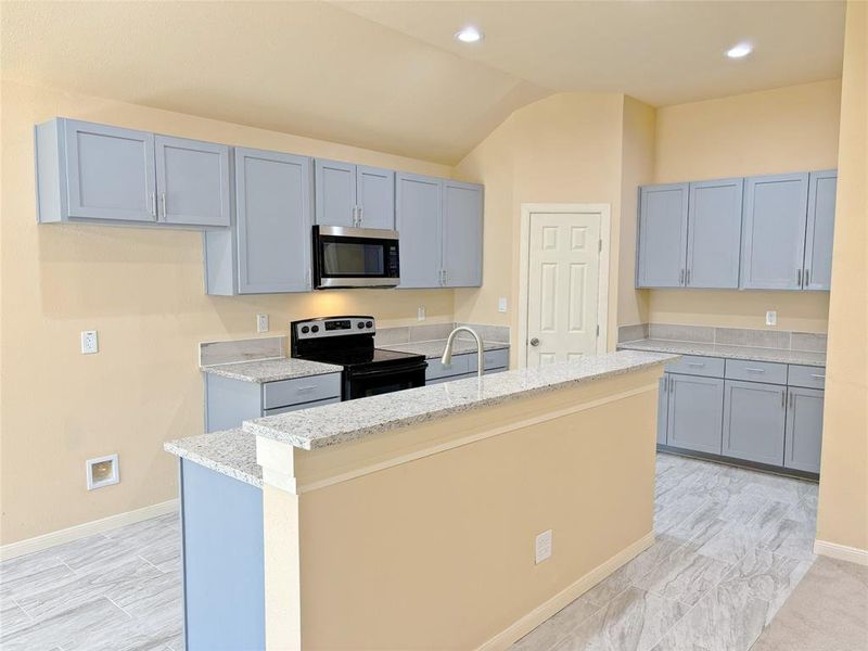 Kitchen featuring an island with sink, range with electric stovetop, stainless steel microwave, light stone counters, and recessed lighting