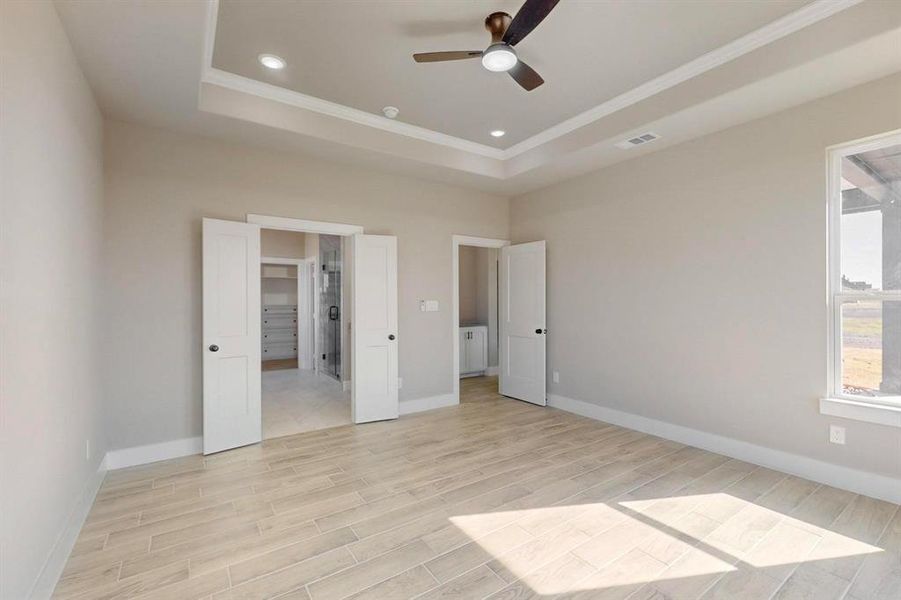 Unfurnished bedroom featuring a raised ceiling, light wood-style flooring, visible vents, and baseboards