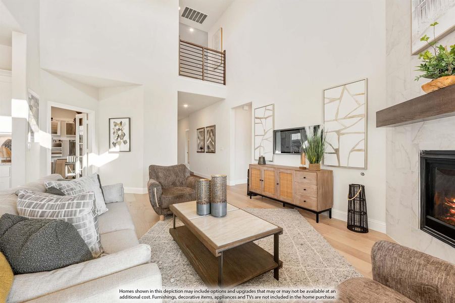 Open living room with two-story ceiling, marble fireplace, hardwood floors, and upper-level railing overlook Open living room with two-story ceiling, marble fireplace, hardwood floors, and upper-level railing overlook