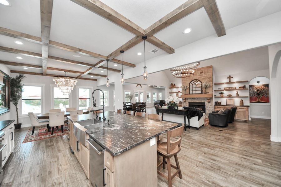 Spacious open-concept living area featuring a gourmet kitchen with a large island, elegant wood-beam ceilings, and a cozy living room with a stone fireplace, perfect for entertaining and family gatherings.