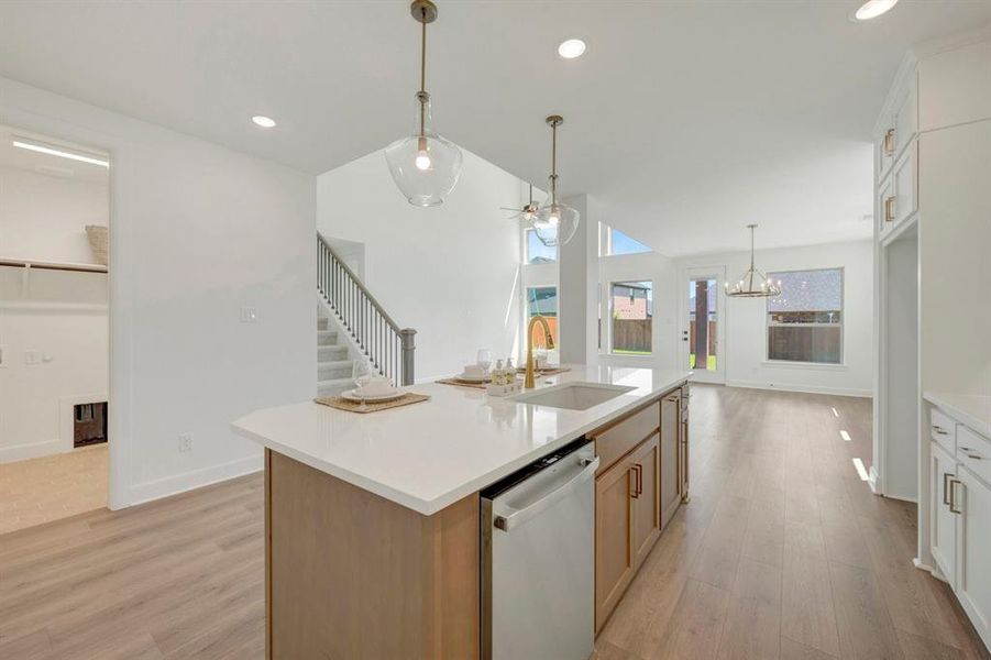 Spacious kitchen island with a white countertop and integrated sink, complemented by pendant lighting, wood-finish flooring, and white cabinetry