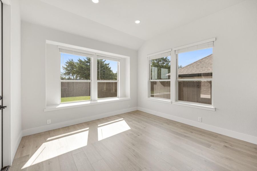Empty room with light wood floors, white walls, and multiple windows with backyard views Empty room with light wood floors, white walls, and multiple windows with backyard views