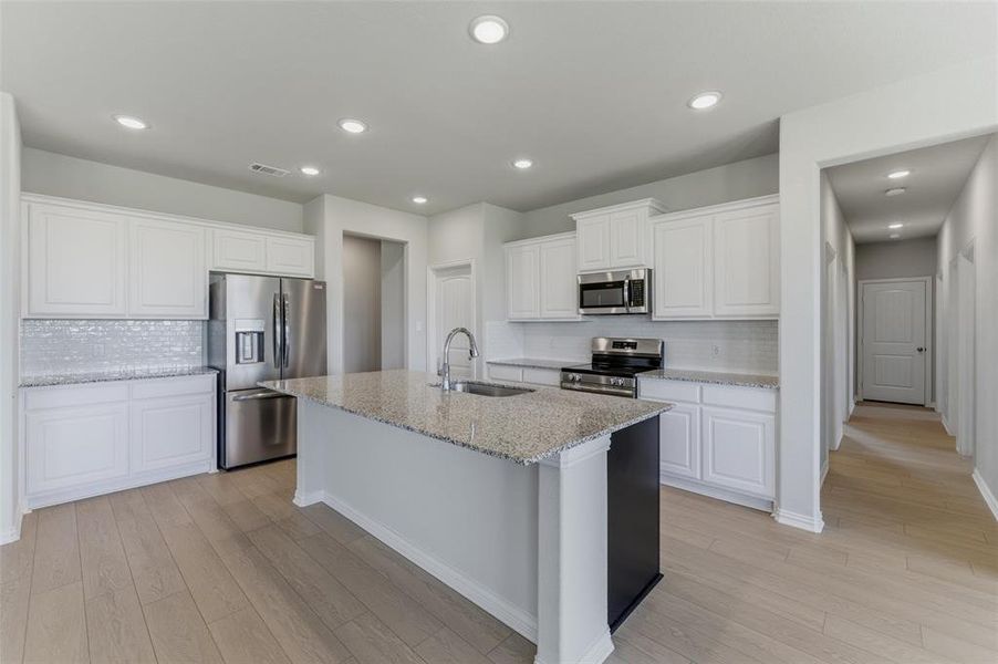 Kitchen featuring an expansive island with a stainless steel sink, granite countertops, white cabinetry, and stainless steel appliances Kitchen featuring an expansive island with a stainless steel sink, granite countertops, white cabinetry, and stainless steel appliances