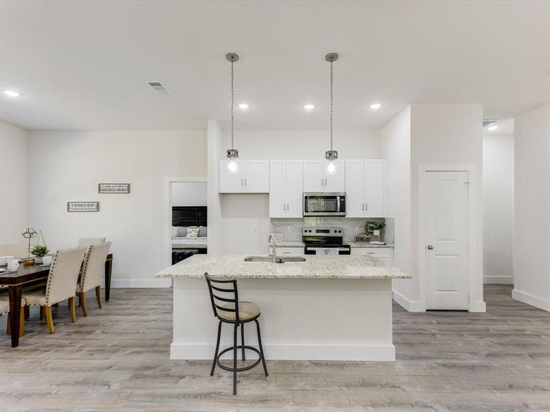 Kitchen featuring tasteful backsplash, hanging light fixtures, white cabinetry, appliances with stainless steel finishes, and light wood-type flooring