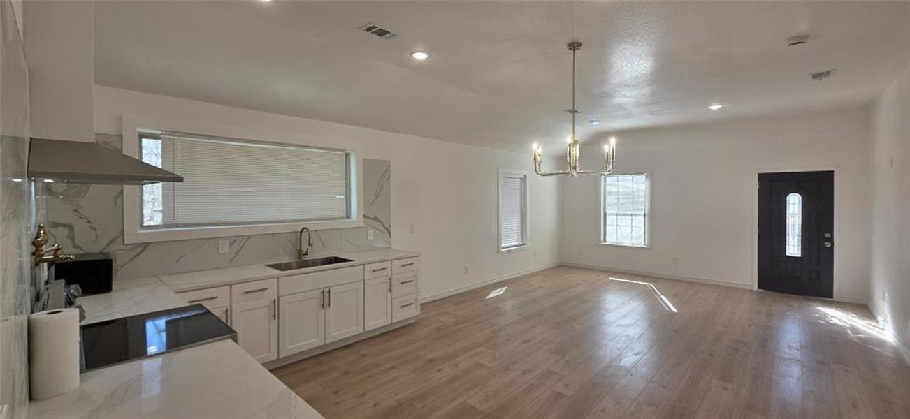 Kitchen with tasteful backsplash, white cabinetry, light stone counters, suspended lighting, and light wood-style flooring