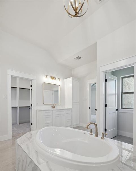 Bathroom with a relaxing tiled tub, vaulted ceiling, sink, tile patterned floors, and a chandelier