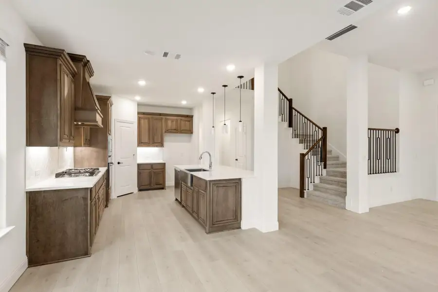 Open kitchen with dark wood cabinets, center island, and light hardwood floors adjacent to staircase Open kitchen with dark wood cabinets, center island, and light hardwood floors adjacent to staircase