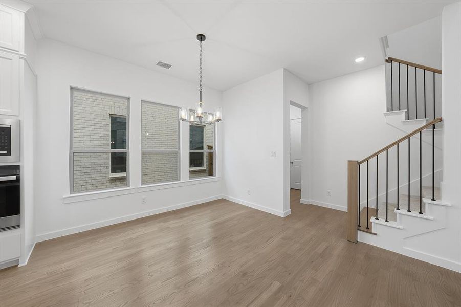 Unfurnished dining area with light wood finished floors, stairs, a chandelier, and recessed lighting