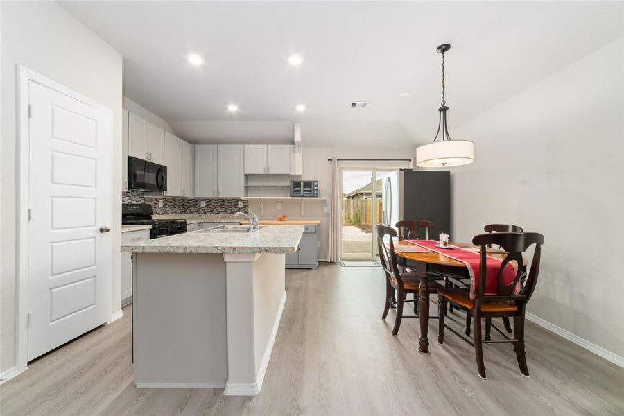 Light-filled kitchen and dining area with high ceilings and recessed lighting, offering an open layout that extends to the backyard through sliding glass doors.