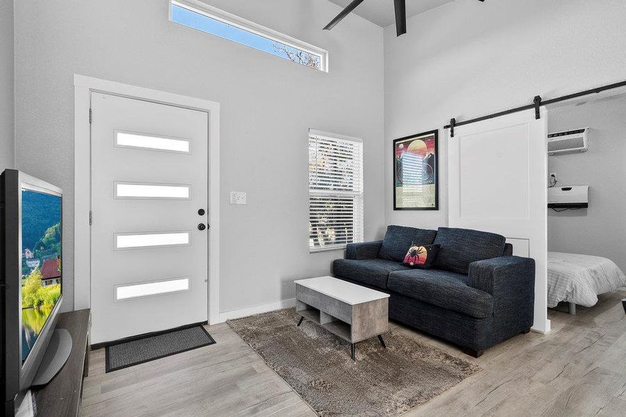 Living area with a barn door, light wood-type flooring, a towering ceiling, and ceiling fan.