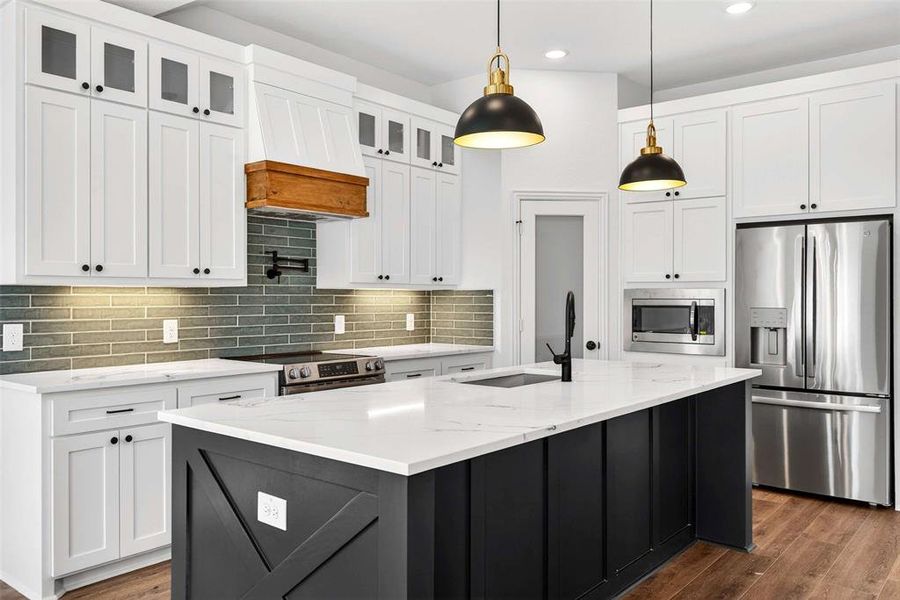 Kitchen with appliances with stainless steel finishes, white cabinetry, a center island with sink, hanging light fixtures, and premium range hood
