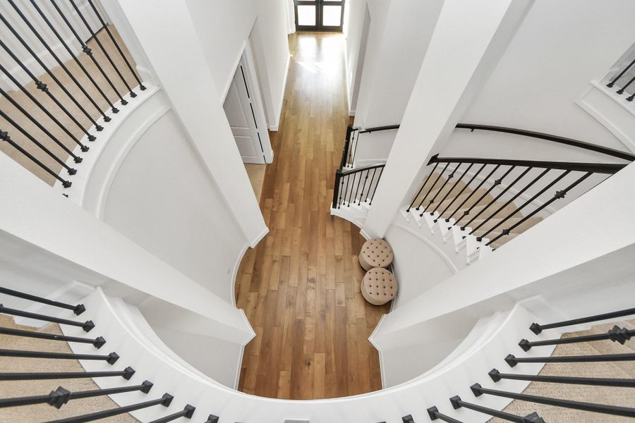 Elegant curved staircase with open railings and upper-level overlook.