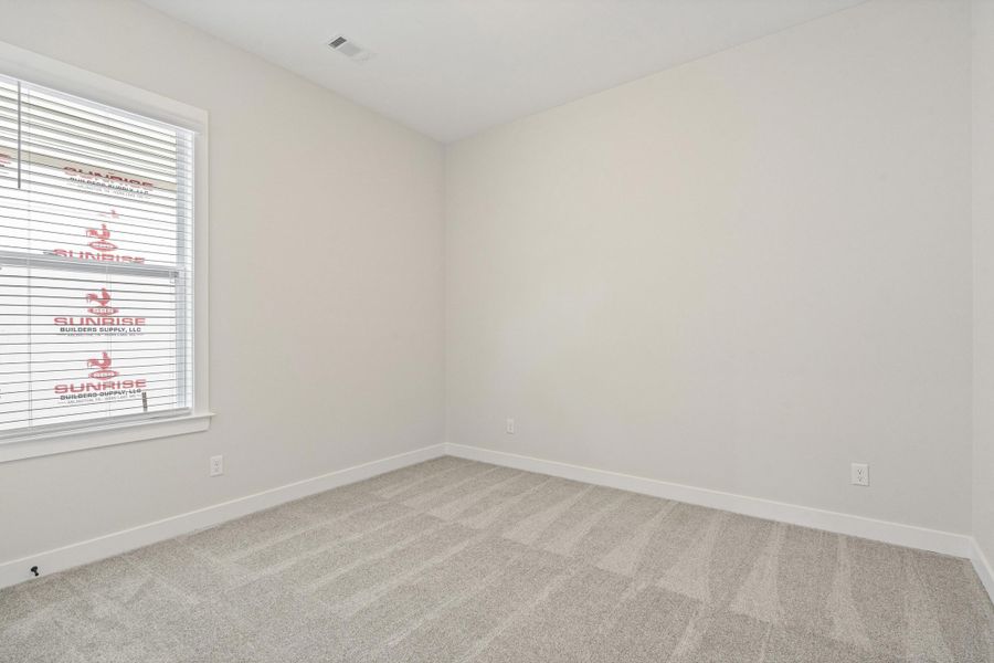 Bright room featuring a window with horizontal blinds, neutral wall tones, and gray patterned carpeting Bright room featuring a window with horizontal blinds, neutral wall tones, and gray patterned carpeting