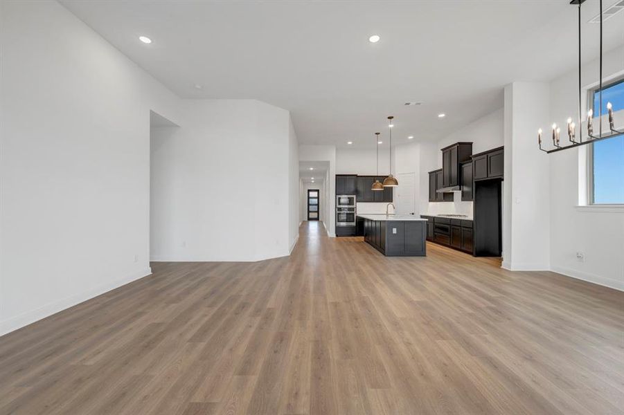 Kitchen featuring open floor plan, a center island with sink, light countertops, light wood-style flooring, and oven