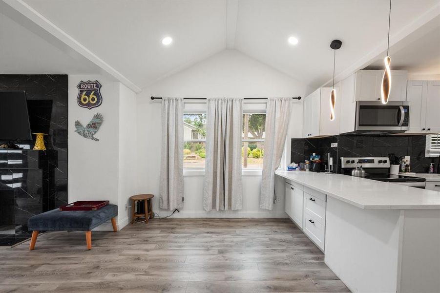 Kitchen featuring appliances with stainless steel finishes, white cabinets, light countertops, vaulted ceiling, and light wood-type flooring Kitchen featuring appliances with stainless steel finishes, white cabinets, light countertops, vaulted ceiling, and light wood-type flooring