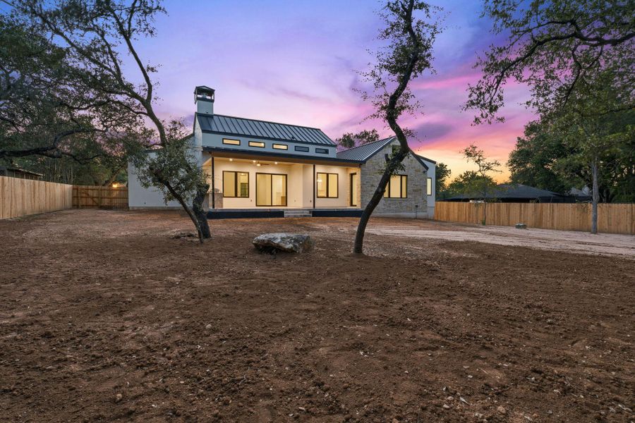 Mature trees frame a modern residence featuring stone accents and a metal roof.