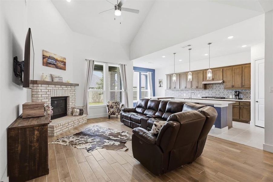 Vaulted ceiling living area featuring a light brick fireplace with a wood mantel
