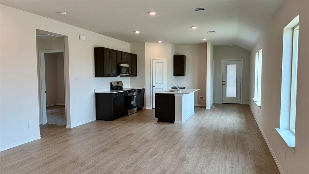 Open-concept kitchen and living area featuring wood-finish flooring, dark wood cabinetry, a central island with white countertops, and stainless steel appliances