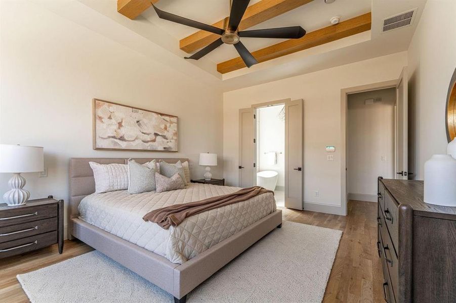 Bedroom with a tray ceiling, ensuite bathroom, ceiling fan, and light wood-style flooring